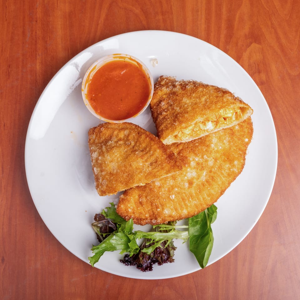 Crispy golden fried turnovers filled with vegetables, served with red dipping sauce and mixed greens on a white plate.